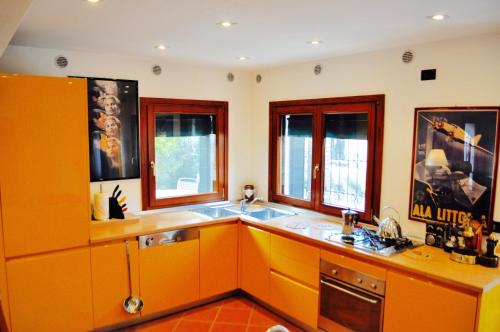 una cocina con armarios naranjas, fregadero y ventanas en La Casa con il Biliardo VeniseJeTaime, en Venecia
