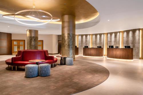 a lobby with a red chair and tables and a chandelier at Hilton Birmingham Metropole Hotel in Bickenhill
