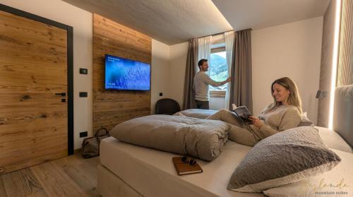 a woman sitting on a bed reading a book at Isolden Green Srl Berlanda Mountain suites in Cavalese