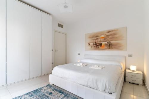 a white bedroom with a white bed and a painting at Elegant Lake View Apartment with Pool in Lavena Ponte Tresa