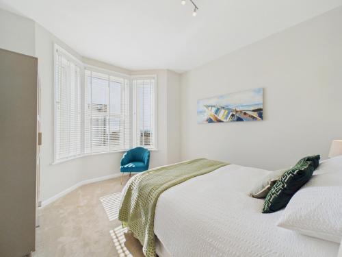 a white bedroom with a bed and a blue chair at Southbourne beach in Southbourne
