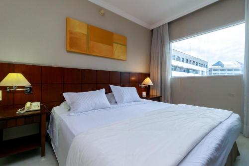 a bedroom with a large white bed and a window at Flat Luxo Verbo Divino 6 in São Paulo
