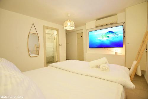 a bedroom with a white bed and a flat screen tv at וילה ארבל in Kefar Weradim