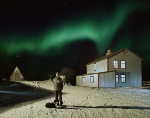 a man standing in the snow under the northern lights at Saudafell Guesthouse in Sauðafell