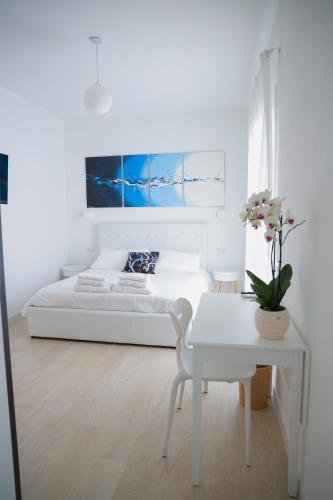 a white bedroom with a bed and a table and flowers at Riganvì Affittacamere Sestu in Sestu
