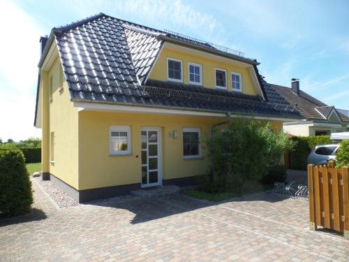 a yellow house with a black roof on a brick driveway at Ferienhaus am Eikboom - DHH1 mit Fasssauna in Ostseebad Karlshagen