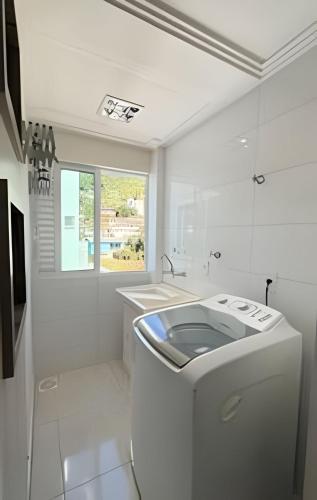 a white bathroom with a sink and a window at Apto Antúrios|3Q. Sacada c/Churrasqueira in Piratuba