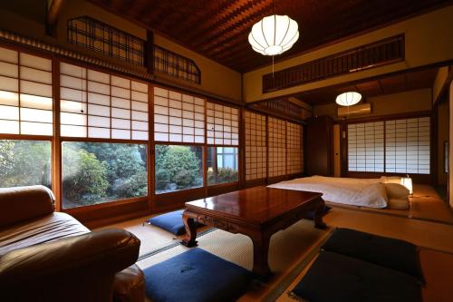 a room with a bed and a table and windows at The Nomad Inn Yugejima in Kami-yuge