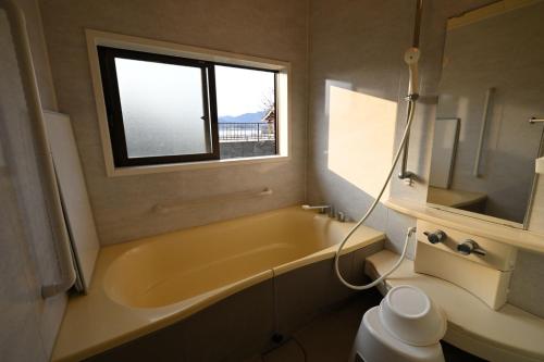 a bathroom with a tub and a sink and a window at The Nomad Inn Yugejima in Kami-yuge
