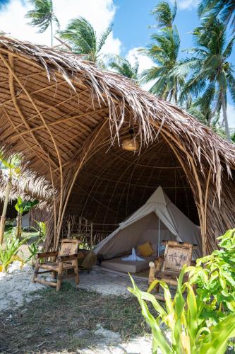 a straw hut with two chairs and a bed and tables at Darocotan Shipwreck Camping in El Nido