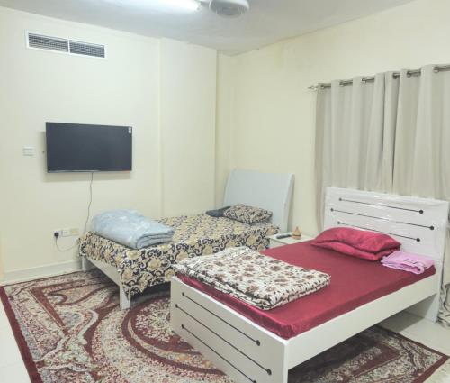 a bedroom with two beds and a flat screen tv at Stay home in ‘Uqayr