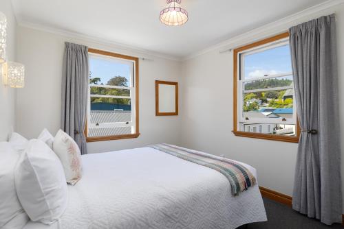 a white bedroom with a bed and two windows at City Apartment South Street in Nelson