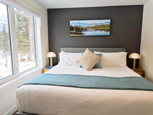 a bedroom with a large bed with two windows at New Luxury MountainView Downtown2B2B RooftopHottub in Canmore