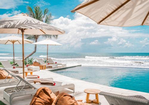 a swimming pool with chairs and umbrellas next to the ocean at Bali Beach Glamping in Tabanan