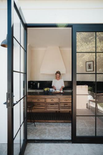 a woman standing in a kitchen looking through a glass door at Blacksmith House on Main in Tocumwal