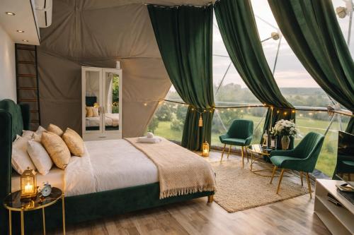 a bedroom with a bed and green chairs and a window at Sun Garden Glamping Domes in Călimăneşti