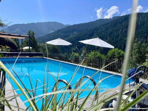 a swimming pool with umbrellas and mountains in the background at ALM SEASONS Premium Chalet & Studios in Saalbach-Hinterglemm