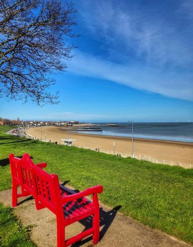 a red bench sitting on the grass near a beach at Rhos on sea home in Llandrillo-yn-Rhôs