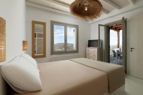 a bedroom with a bed and a tv and windows at West Side Pool House by Hostandros in Gavrio