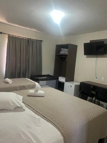 a hotel room with two beds and a desk at HOTEL SAYMON - Cafelândia PARANÁ in Cafelândia