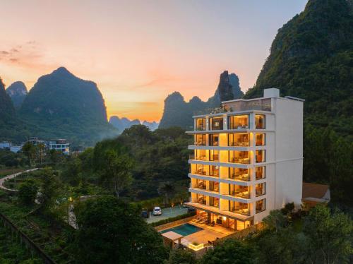 a hotel building with mountains in the background at Yangshuo Xishan Resort in Yangshuo