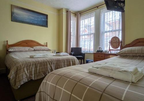 a bedroom with two beds and a desk and windows at Kingswinford Guest House with Free Parking in Paignton
