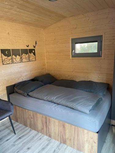 a bed in a wooden cabin with a window at maringotky Šumava in Dlouhá Ves