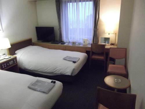 市川市にある市川グランドホテルのベッド2台とデスクが備わるホテルルームです。