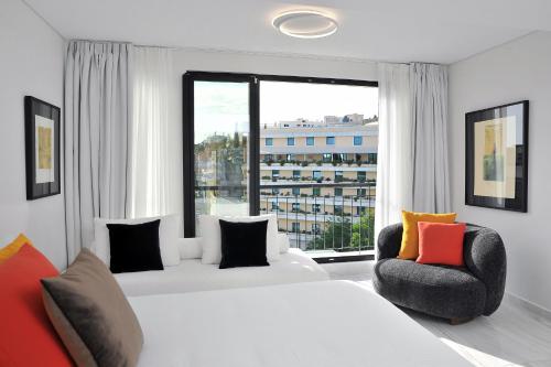 a bedroom with two beds and a chair and a large window at The Athenaeum Luxury Hotel in Athens
