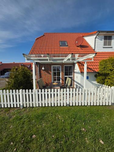 a white fence in front of a house with a red roof at Ferienhaus Seemöwe mit Deichblick Butjadingen-Burhave in Burhave