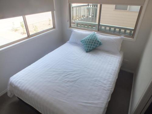 a small bedroom with a white bed with two windows at Albury Gardens Tourist Park in Lavington