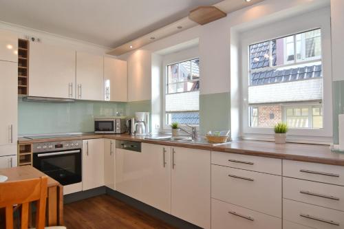 a kitchen with white cabinets and a table and two windows at Wodan, Whg 1 in Tinnum