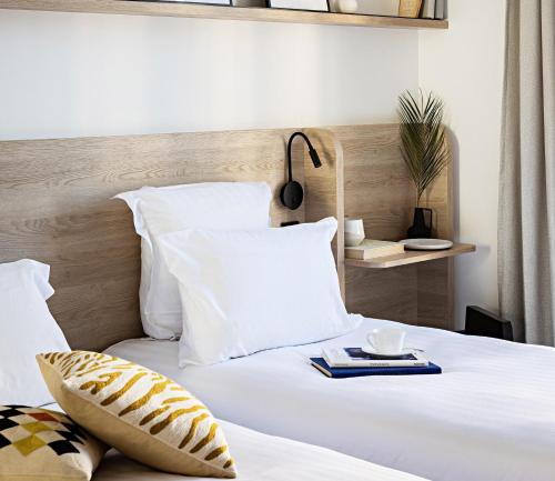 ein Bett mit weißen Kissen und einem Buch darauf in der Unterkunft Le Riviera Collection, Signature Collection by Best Western in Nizza