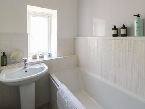 a white bathroom with a sink and a bath tub at Castle Gardens Apartment in Beaumaris