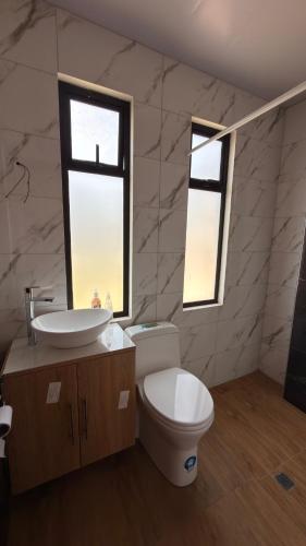 a bathroom with a toilet and a sink and two windows at Casa moderna, amplia y acogedora Valentina in Loja