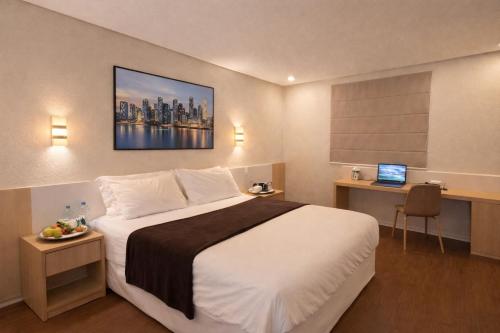 a hotel room with a bed and a desk with a laptop at Hotel Thomasi Express in Maringá