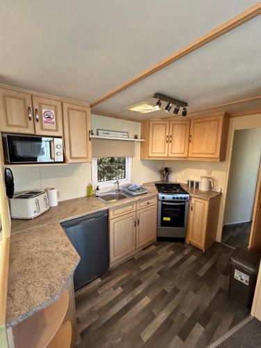 a kitchen with wooden cabinets and a stove top oven at Bailey's Caravan Hire - Sealands Plot 1 - Wi-Fi - Dog Friendly in Ingoldmells