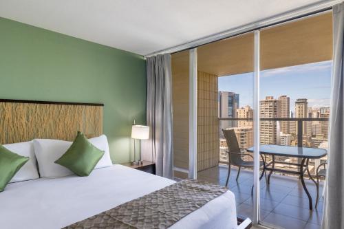 a bedroom with a bed and a balcony with a table at Skyline Island Colony Hotel in Honolulu