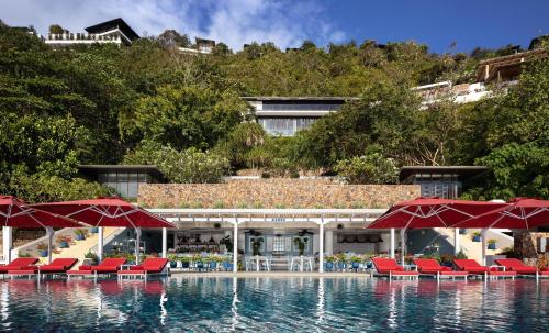 a swimming pool with chairs and red umbrellas at Conrad Koh Samui in Taling Ngam Beach