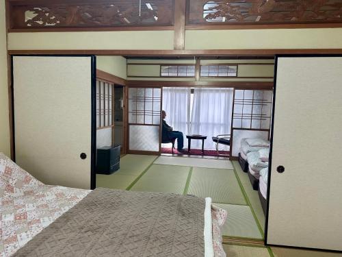 a bedroom with a bed and a person sitting in a window at Tora House in Nagoya