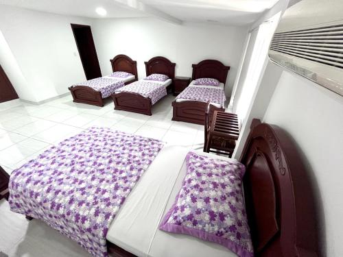 three beds in a room with purple blankets at Hotel Exelsior in Cúcuta