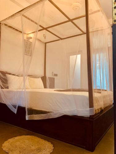 a canopy bed with white sheets and pillows at Thaproo Bay Hiriketiya in Dickwella