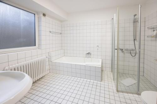 a white tiled bathroom with a tub and a shower at Hotel Am Martinsberg in Andernach