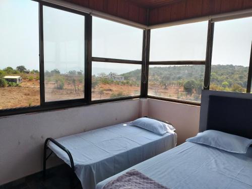 two beds in a room with large windows at Sattva Gruha in Māngaon
