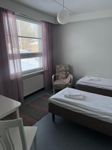 a room with two beds and a chair and a window at Hostelli Palonkortteeri in Ilmajoki
