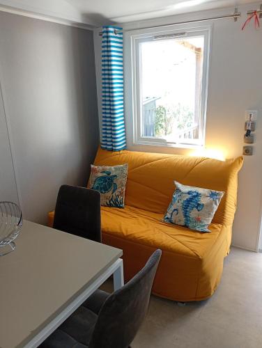 a living room with a yellow couch and a window at Mobile-Home L'Instant Marin in Sérignan