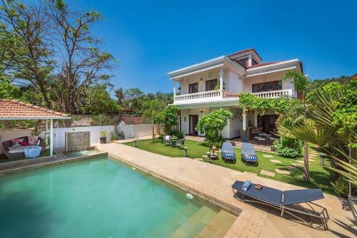 a house with a swimming pool in front of a house at SaffronStays Sweet Mango - 4BR Goan Villa w Private Pool, Mango Garden, Bar Gazebo & Vibrant Interiors Near Beaches in Parra