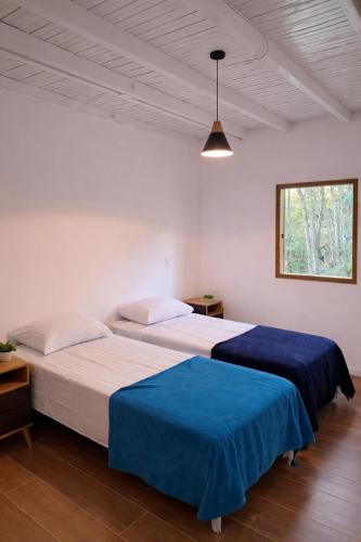two beds in a white room with blue sheets at Chalé Pedra Furada in Resende