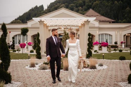 a bride and groom walking in front of a mansion at Grădina Mariajelor Hotel in Câmpulung Moldovenesc