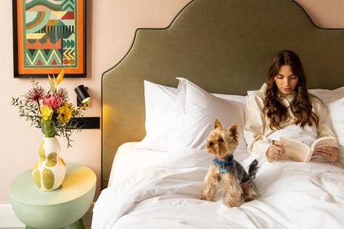 a woman sitting in bed reading a book with a dog at The Mila Porto in Porto